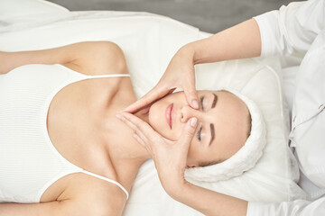 Caucasian female receiving facial massage in spa with therapist s hands on face in relaxing atmosphere.