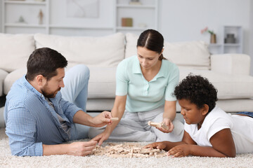 Adoption. Parents and their son playing with wooden blocks on floor at home