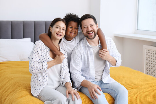 Adoption. Happy parents and their son on bed at home
