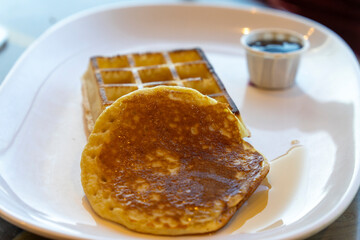 Waffle and pancake on white plate chocolate dip in background