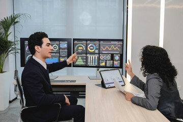 Business professionals analyzing data and discussing financial reports with digital dashboards and graphs in a modern office setting, focusing on strategy and performance.