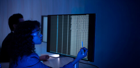 Two software developers collaborating at night, focusing on code review and debugging process on a computer screen, representing teamwork, innovation, and modern software development workflow.