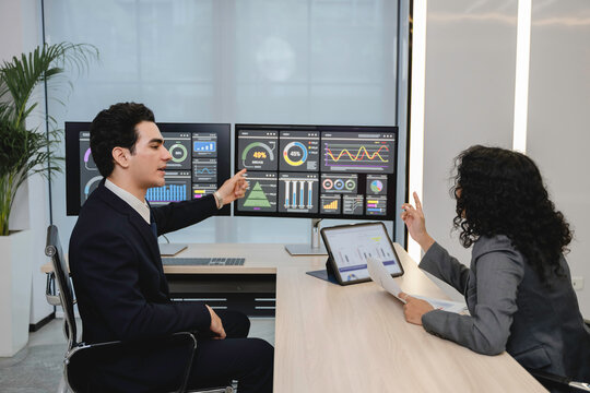 Business professionals analyzing data and discussing financial reports with digital dashboards and graphs in a modern office setting, focusing on strategy and performance.