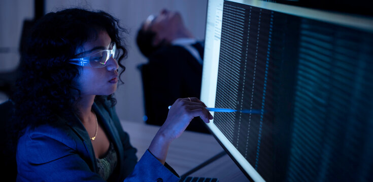 Two software developers collaborating at night, focusing on code review and debugging process on a computer screen, representing teamwork, innovation, and modern software development workflow.