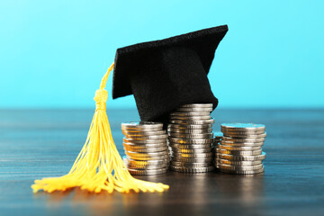 Scholarship. Graduate hat and coins on wooden table against light blue background, closeup