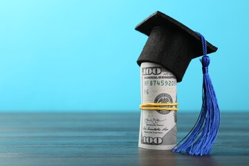 Scholarship. Graduate hat and dollar banknotes on wooden table against light blue background,...