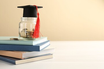 Scholarship. Jar with graduate hat, coins and books on white wooden table against beige background,...