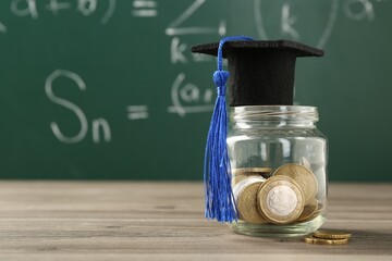 Scholarship. Jar with graduate hat and coins on wooden table against green chalkboard, closeup....