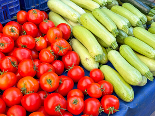 Red tomatoes and light green zucchinis arranged side by side on market stall. Agriculture, farming, and seasonal vegetable harvest with nutrition and lifestyle.