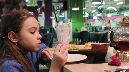 satisfied girl, enjoys delicious meal, holds piece of pizza, has snack dressed in jacket, spends...
