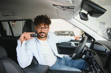 Happy man showing car key sitting in new vehicle in dealership