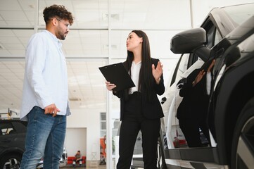 Saleswoman showing new car to customer in dealership
