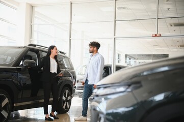 Saleswoman showing new car to customer in dealership