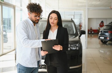 Saleswoman showing contract to customer buying new car in dealership
