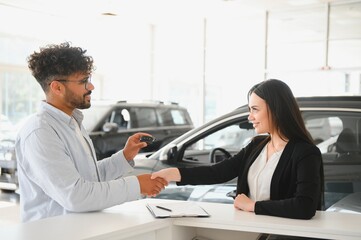 Saleswoman shaking hands with customer buying new car at dealership