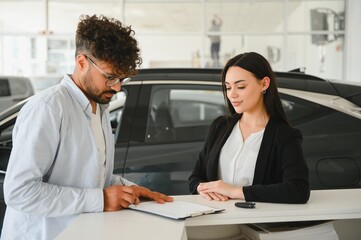 Customer signing contract for new car in dealership with saleswoman