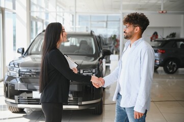 Saleswoman shaking hands with customer buying new car in dealership