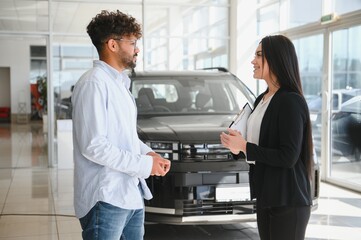 Saleswoman showing new car to customer in dealership
