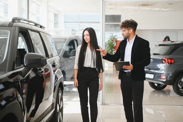 Car salesman showing a new vehicle to a businesswoman in a dealership
