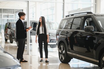 Car salesman showing new vehicle to female customer in dealership