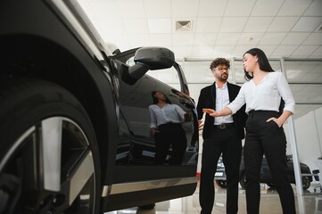 Car salesman showing a new car to a female customer in dealership