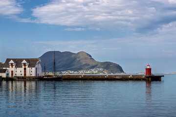 Paisaje marino de un barco, una casa, un faro y una montaña al fondo en Alesund, Noruega