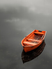 Obraz premium A tiny orange wooden boat drifts quietly on still gray water, creating a calm, minimalist, and contemplative natural scene.
