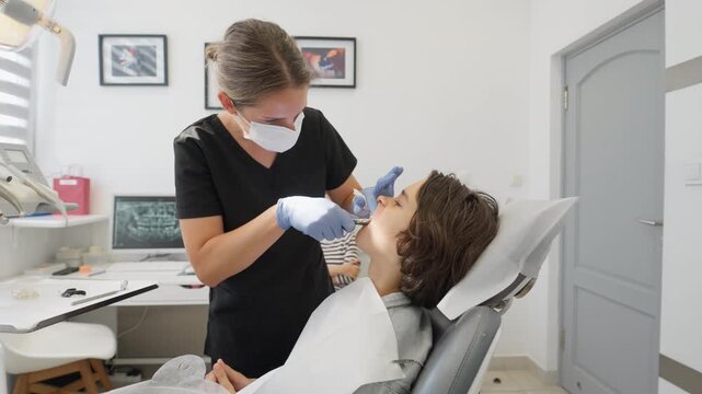 A pediatric dentist performs a tooth extraction using surgical forceps on a teenage boy. This dental surgery is for removing a primary (milk) tooth as part of a treatment plan in a clinic.