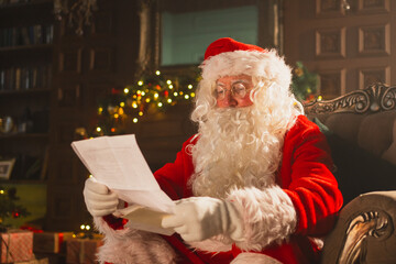 Merry Christmas. Happy Santa Claus reading letters from children in festive Christmas living room....