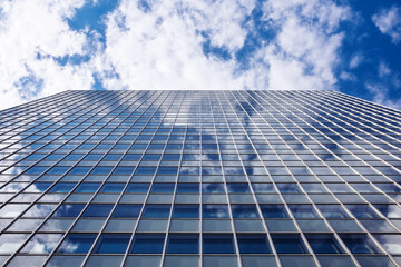 Obraz premium Glass facade of a modern skyscraper reflecting clouds and blue sky in an upward perspective