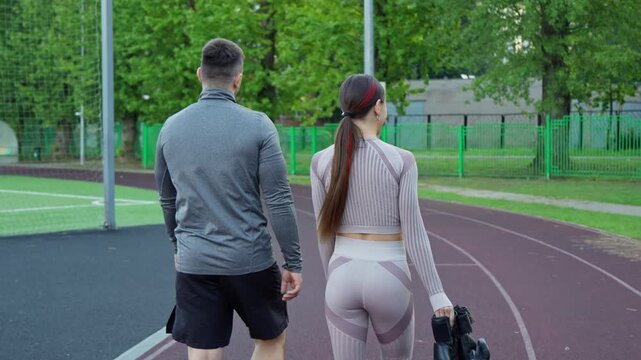 Man and woman walking at sports track in early morning. Box training. Healthy lifestyle concept. Boxer woman trains with male partner. Back tracking shot. 4K, UHD