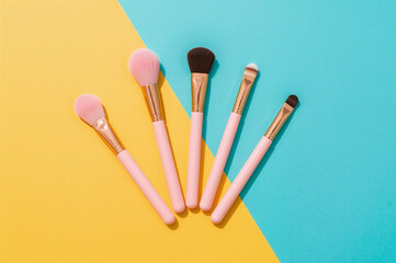 Top down flat lay of five pink makeup brushes against a pastel background product photography