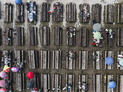 Aerial view of rustic wooden picnic tables aligned in perfect rows, dotted with colorful umbrellas and people enjoying an outdoor meal, Gran Sasso, Abruzzo, Italy.