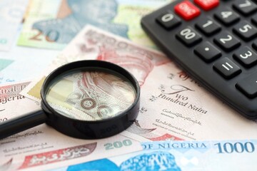 Nigerian naira currency money bills and calculator with magnifying glass. The concept of taxation and money count