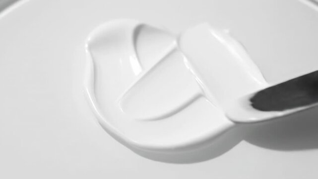 White Cream Texture Swirl - Close-up shot of a metallic spatula spreading white cream, showcasing its smooth and luxurious texture. The video highlights the cream's consistency and its subtle shine.