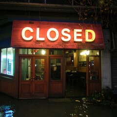 A neon sign that says CLOSED illuminates a storefront at night.