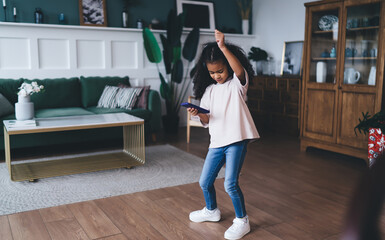 Joyful African American girl dancing with headphones and smartphone, celebrating music and...