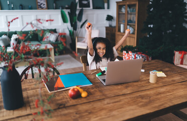 Excited African American girl celebrating success while sitting at laptop. Concept of online learning achievement, motivation, and fun with educational technology