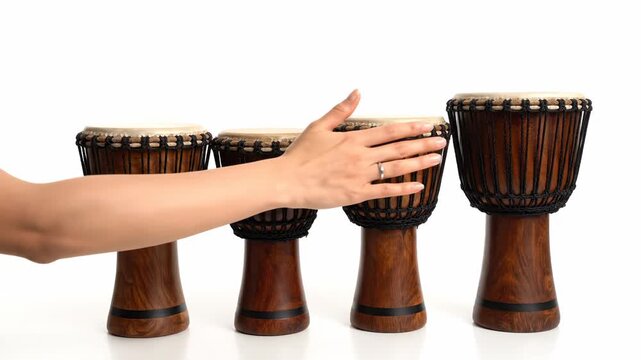 Hand Reaching for Traditional Drums - A hand gently reaches towards a row of four traditional hand drums, showcasing their rich wood tones and intricate detailing against a clean white background.