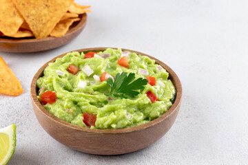 Mexican guacamole with tomatoes, jalapenos and crispy tortilla chips on a white background. Mexican food.