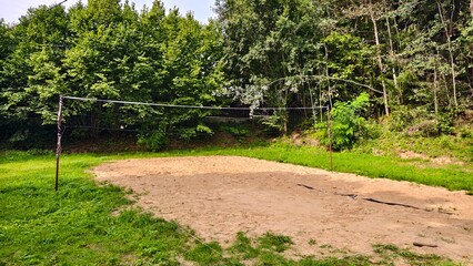 A sand volleyball court with metal posts and net is located on a grassy lawn and surrounded by...