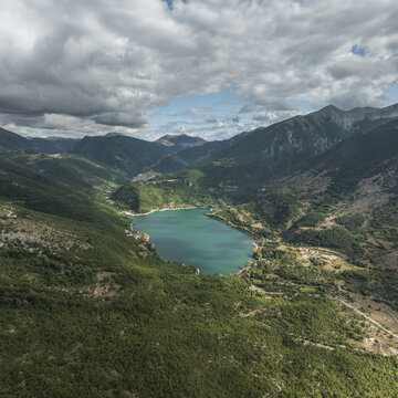 Aerial view of a serene turquoise lake nestled between verdant mountains under a dramatic sky in Contrada Frattura, Frattura Vecchia, Abruzzo, Italy.