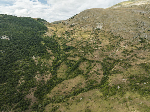 Aerial view of the verdant forests meeting the arid mountainside in a tapestry of green and brown, Contrada Frattura, Abruzzo, Italy.