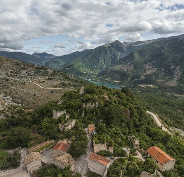 Aerial view of ancient ruins nestled amidst lush greenery, with a tranquil lake reflecting the sky beyond, Contrada Frattura, Frattura Vecchia, Abruzzo, Italy.