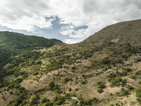 Aerial view of the contrasting green and brown hillsides meeting under a vast sky, Contrada Frattura, Abruzzo, Italy.