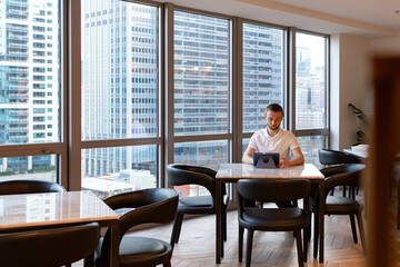 Happy confident mature business man sitting in coworking using digital tablet. Smiling European student wearing light shirt doing study online