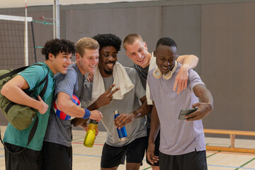 Diverse male friends posing for selfie on volleyball court with smartphone, volleyball