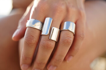 Close-up of a hand wearing modern minimalist silver rings with geometric shapes, polished surfaces reflecting light, stylish jewelry detail in natural daylight