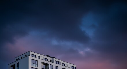 Corner of a modern white apartment building under a dramatic purple and blue twilight sky.