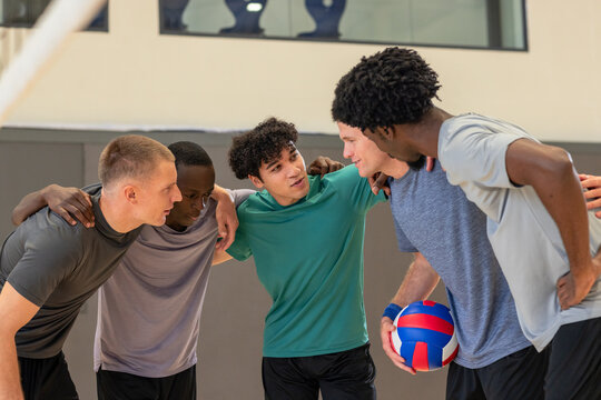 Diverse male partners huddling together sharing pre-game strategy on gym court with volleyball - Powered by Adobe